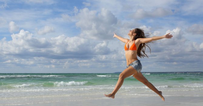 радостная девушка без признаков ожирения бежит по пляжу вдоль моря на фоне волн